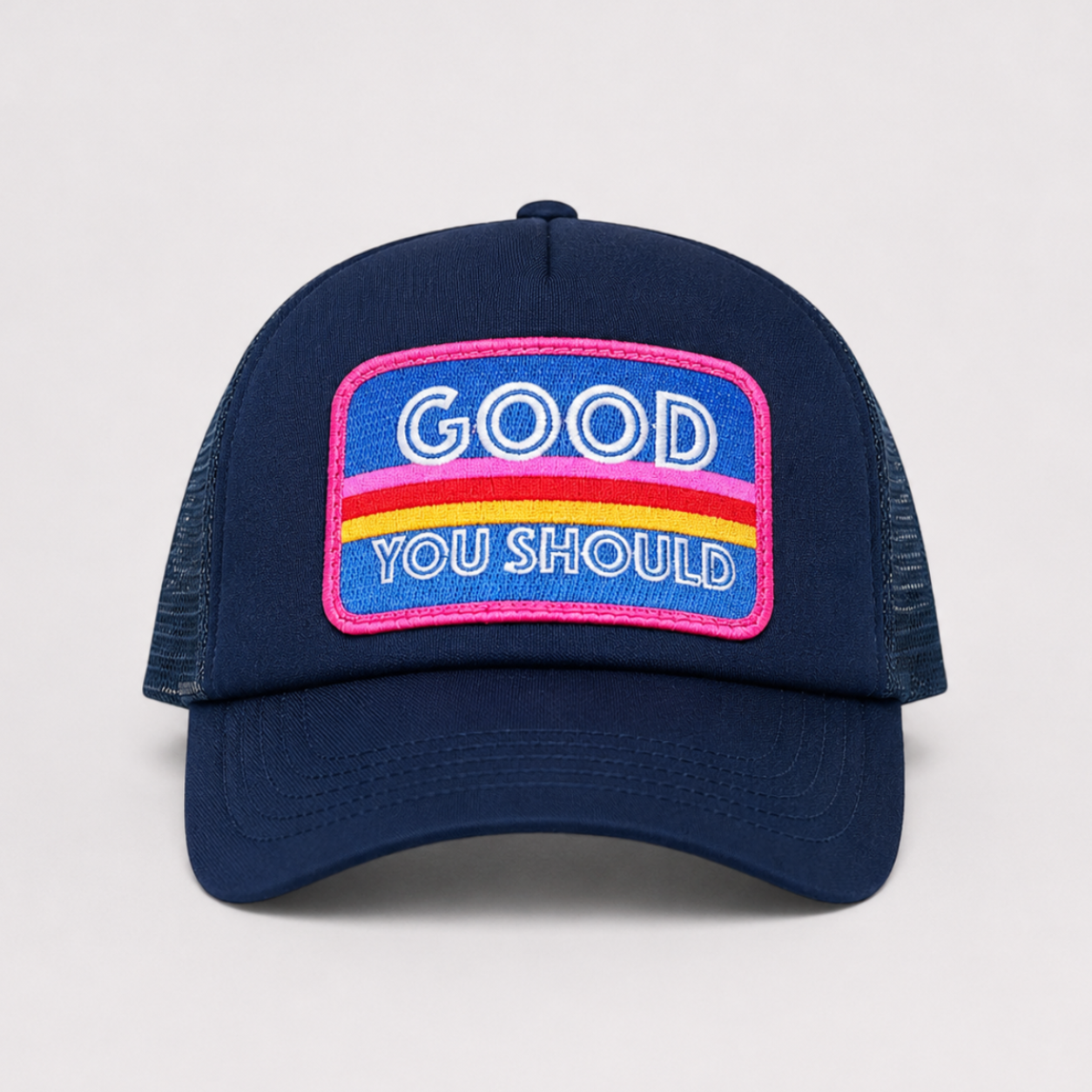 A navy blue trucker hat with a curved brim and mesh back, featuring a colorful embroidered patch on the front that reads 'GOOD YOU SHOULD' in white text over pink, purple, and yellow stripes.