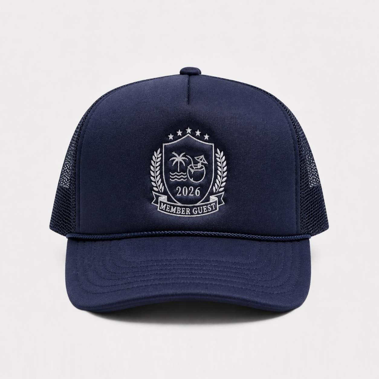 A navy blue trucker hat with a white embroidered crest on the front panel. The crest features palm trees, a coconut, the year '2026', and a banner reading 'MEMBER GUEST'.